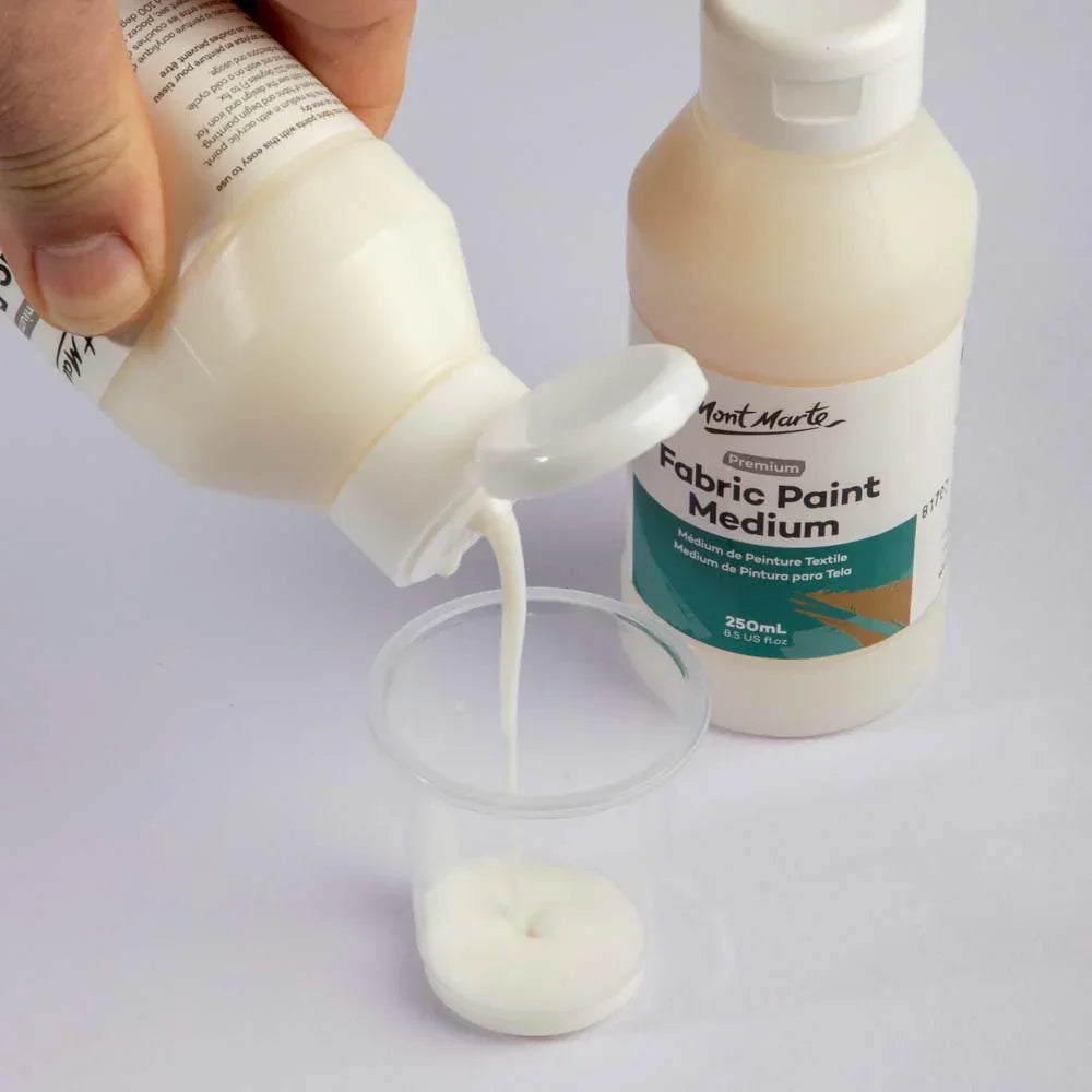 Mont Marte Fabric Paint Medium 250ml bottle being poured into a clear plastic cup