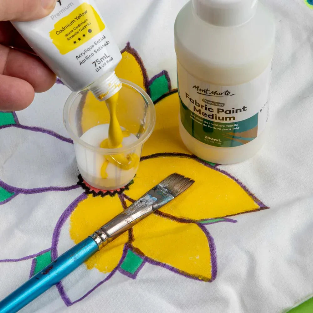 Mont Marte Fabric Paint Medium bottle, yellow paint mixing, brush, and painted flower on fabric