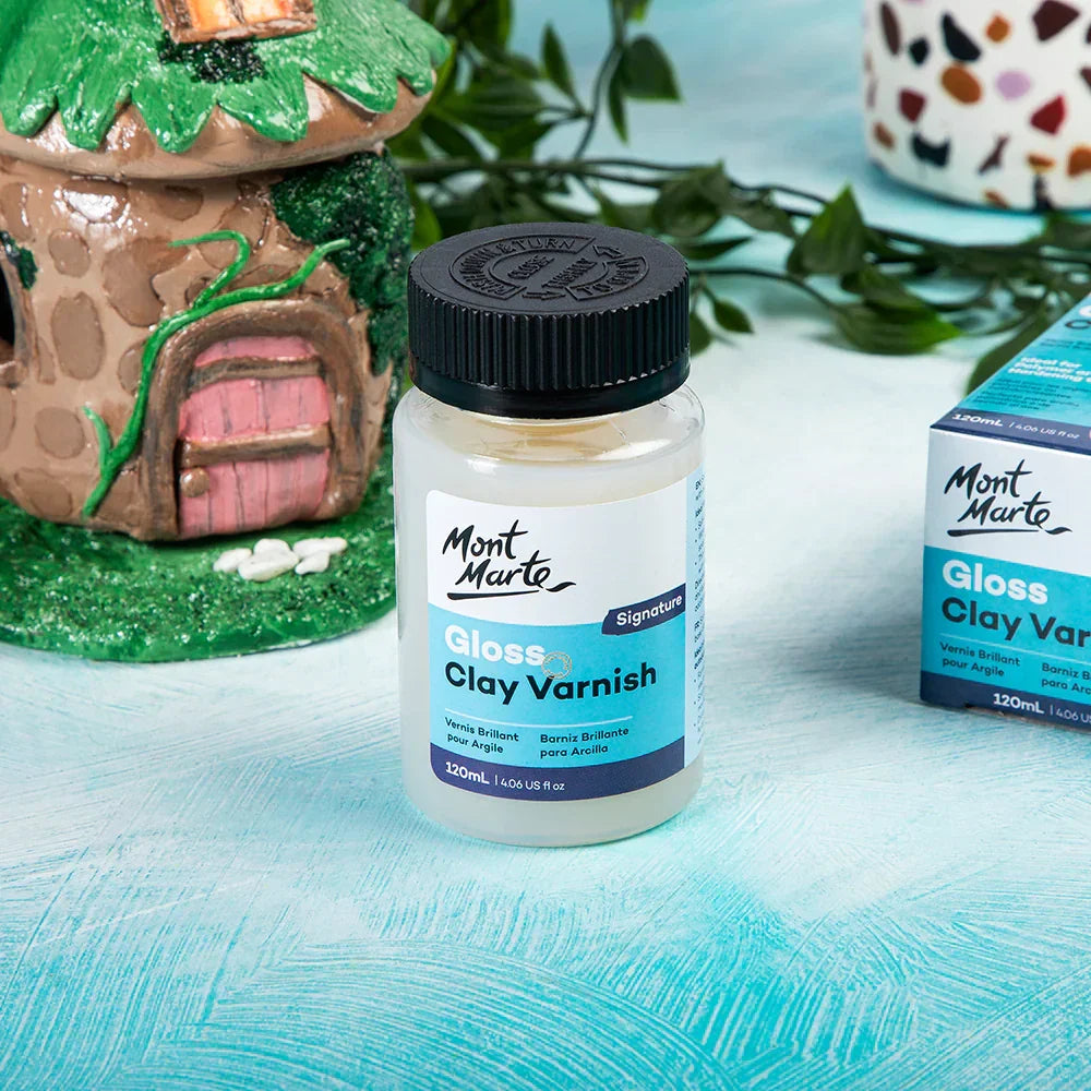 Mont Marte Gloss Clay Varnish 120mL bottle on a blue surface with clay art in the background