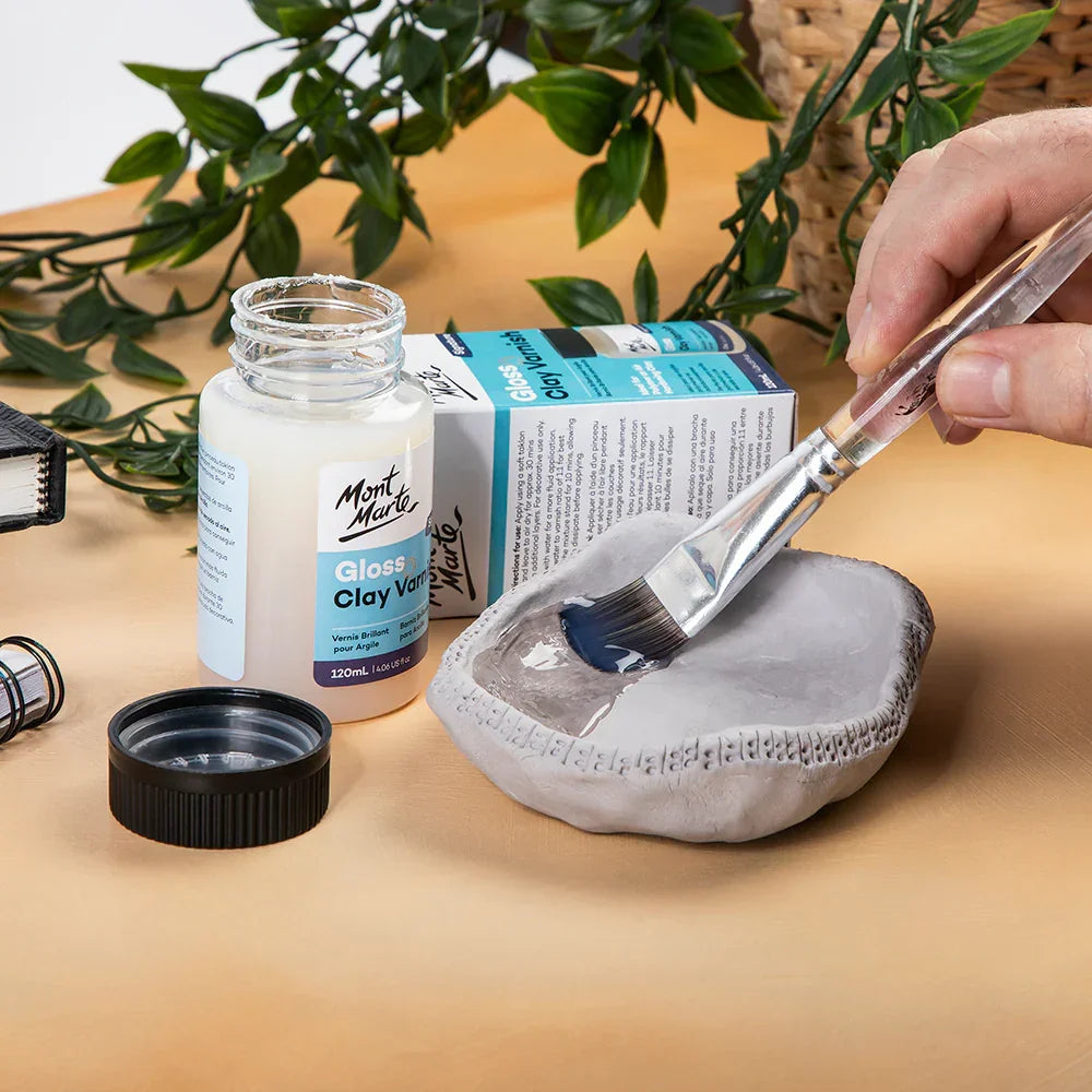 Mont Marte Gloss Clay Varnish being applied with a brush to a small clay dish on a table